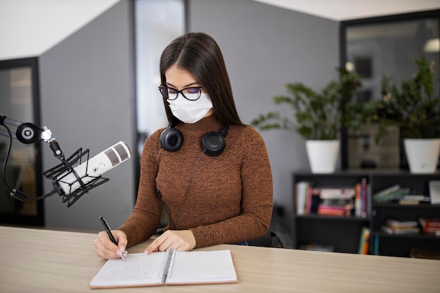 Woman with medical mask on the radio with microphone and notebook