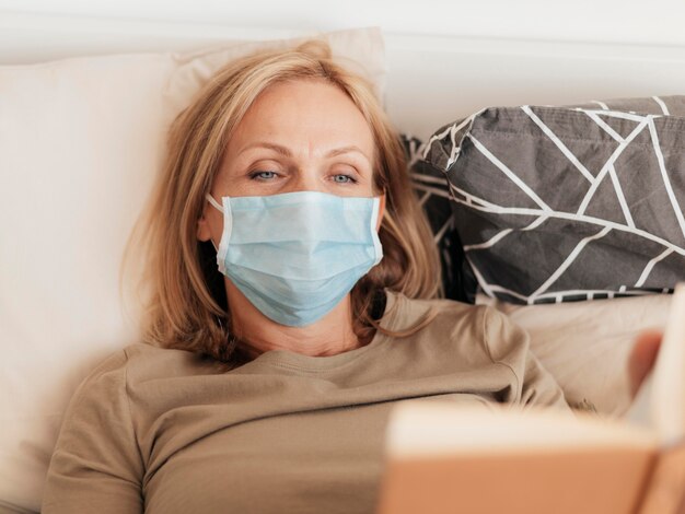 Woman with medical mask reading book in quarantine