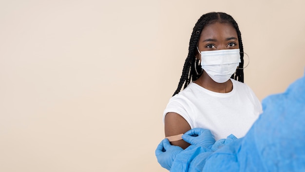Бесплатное фото Женщина с медицинской маской получает наклейку на руку после вакцинации