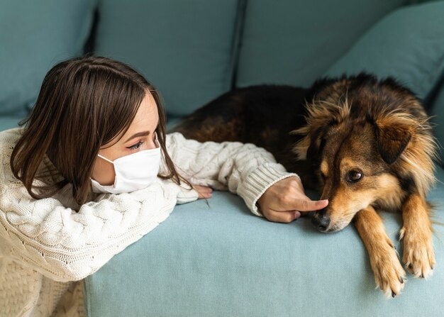 自宅でのパンデミックの最中に犬の隣に座っている医療用マスクを持った女性