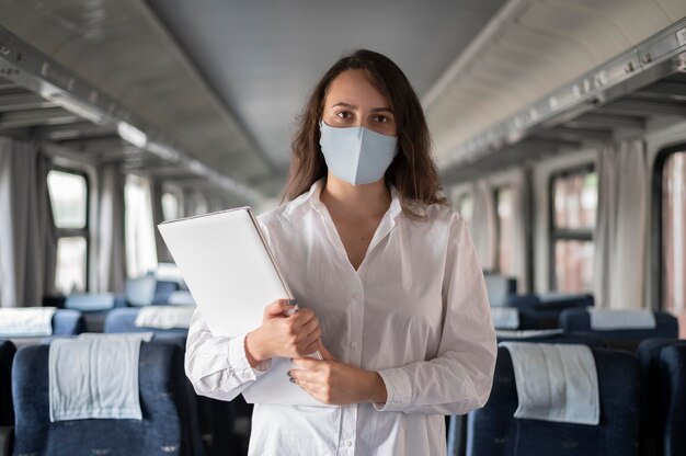 Woman with medical mask traveling by public train and using laptop