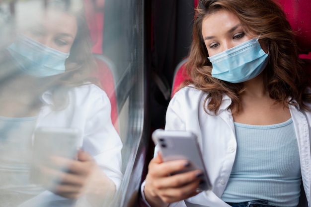 Woman with medical mask traveling by public train and using smartphone