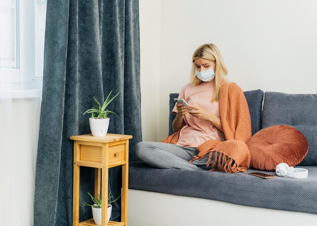 Foto gratuita donna con mascherina medica utilizza lo smartphone a casa durante la pandemia