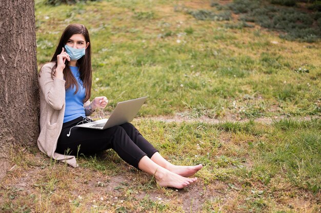 Woman with medical mask working on laptop outdoors