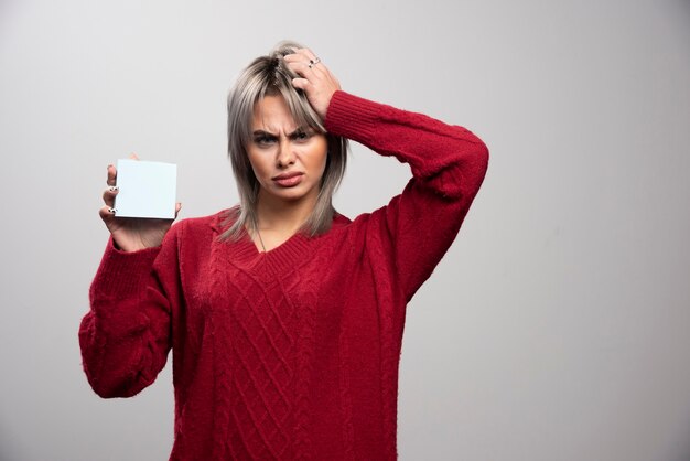 Woman with memo pad looking angry on gray background.