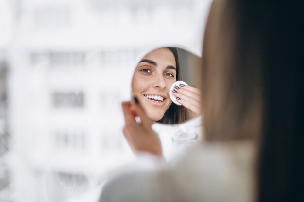 Woman with mirror removing makeup with pad