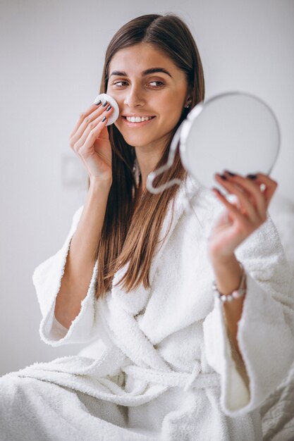 Woman with mirror removing makeup with pad