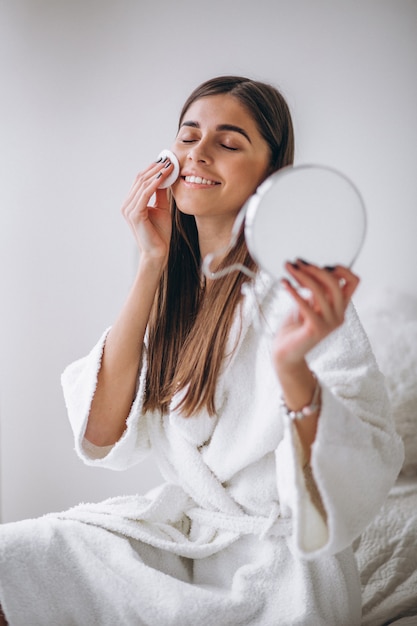 Woman with mirror removing makeup with pad