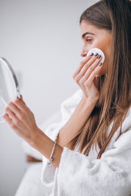 Woman with mirror removing makeup with pad