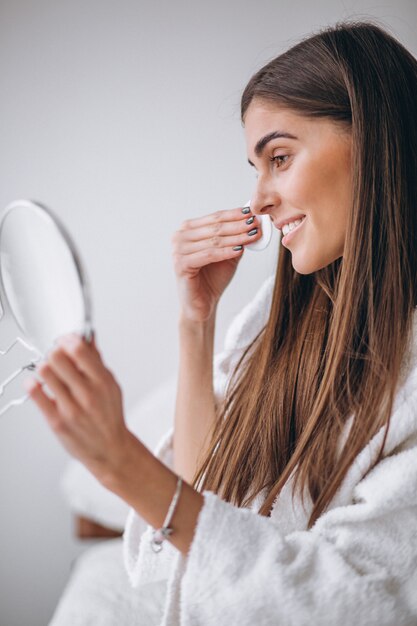 Woman with mirror removing makeup with pad