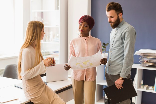 Woman with mug near colleagues with blueprint