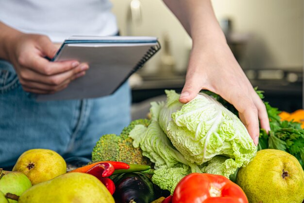 Foto gratuita donna con blocco note e verdure sul tavolo della cucina che prepara una ricetta