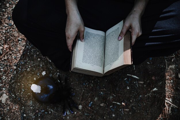 Woman with opened book and candle on forest ground