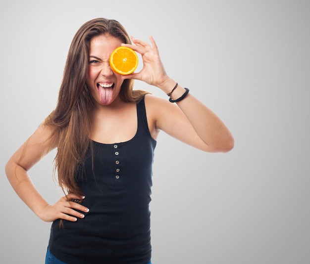 Woman with orange half on one eye and tongue out