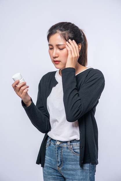 A woman with pain in her hand holds a medicine bottle and the other hand but on her head