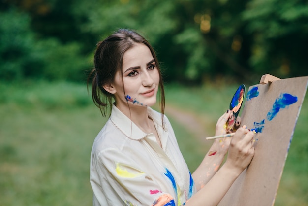 Woman with painted colorful face drawing on a canvas