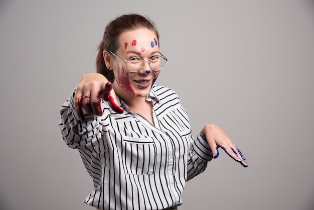 Free photo woman with paints on her face and glasses on gray background