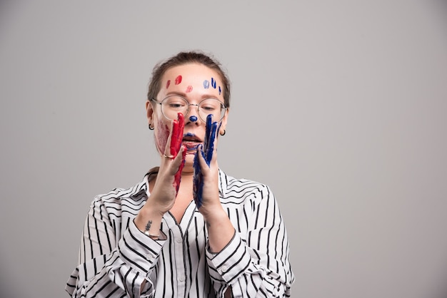 Woman with paints on her face and glasses on gray background