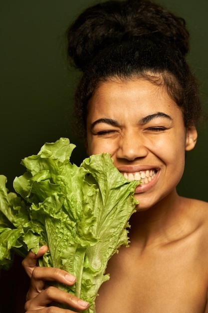Бесплатное фото Женщина с идеальной кожей кусает зеленый салат, позирует с закрытыми глазами, изолированными на зеленом