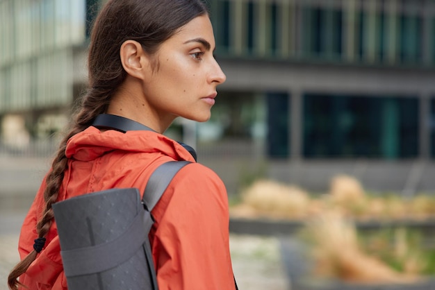 Woman with pigtail dressed in anorak keeps healthy has regular training uses sport accessories looks away concentrated into distance poses outdoors outdoor