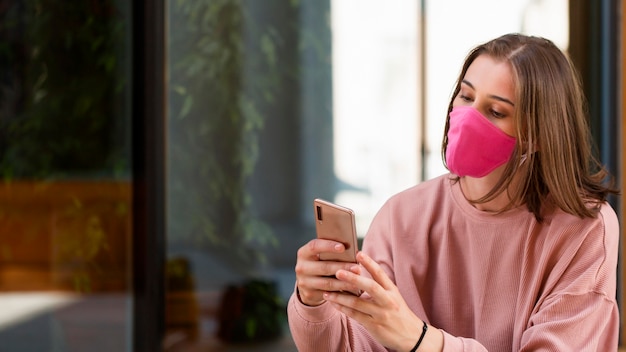 Бесплатное фото Женщина с розовой маской держит смартфон