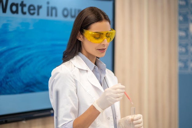 Woman with pipette over test tube standing in classroom