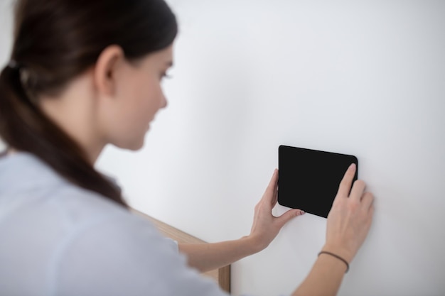 Woman with a ponytail attaching a gadget to the vertical surface