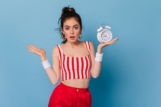 Free photo woman with ponytail and nude make-up surprised looking at front on blue wall