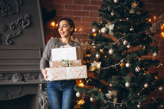 Женщина с подарками стоит перед елкой