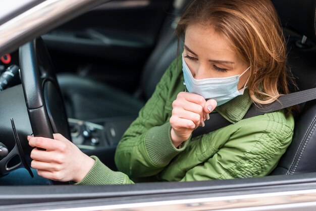 彼女の車の咳で保護マスクを持つ女性