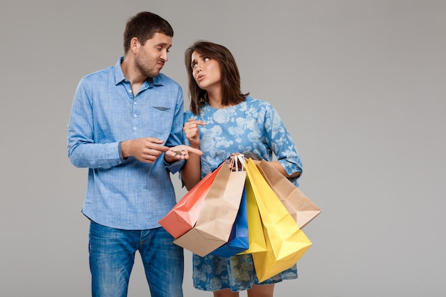 Woman with purchases, man holding last money over grey wall