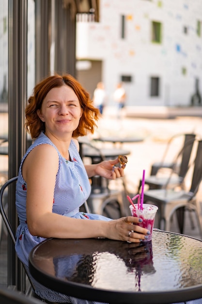 женщина с рыжими волосами в кафе пьет летний коктейль, счастлива, смеется, улыбается.