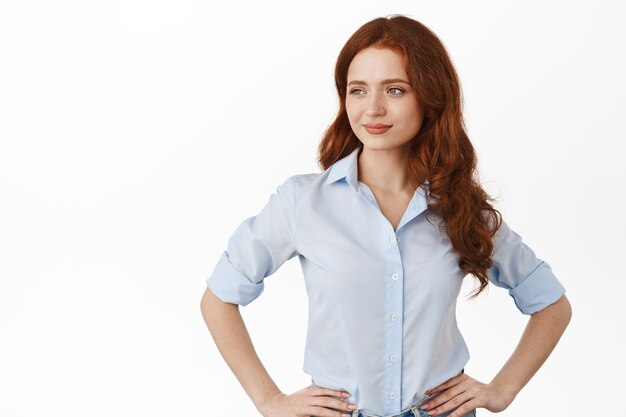 woman with red hair, hold hands on waist, looking aside pleased and confident, manage business, standing self-assured on white