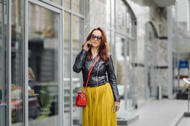 Woman with red handbag walking while speaking on the phone near a business building