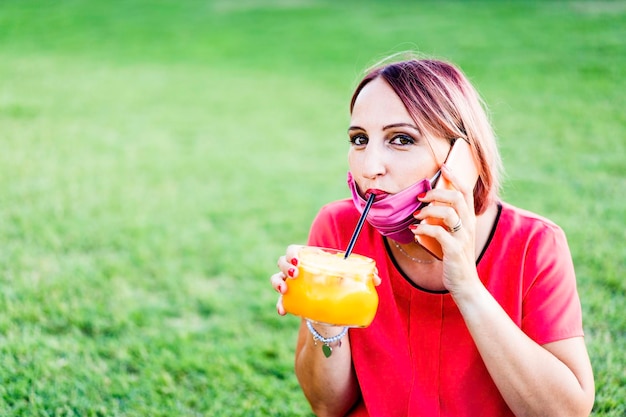 복고풍 병 야외에서 오렌지 주스를 마시는 빨간 립스틱과 장미 염색 머리를 가진 여자 갓 짜낸 오렌지를 마시는 여름 칵테일을 마시는 건강한 식단과 건강한 생활 방식 개념 복사 공간