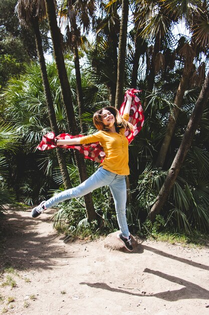 Woman with red scarf jumping near palms