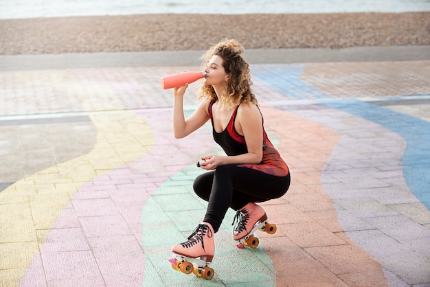 Женщина с роликовыми коньками пьет воду на открытом воздухе