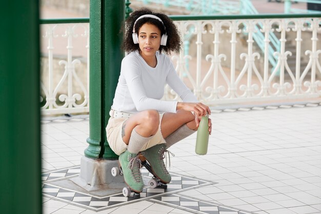 Woman with roller skates listening to music and opening a bottle of water outdoors