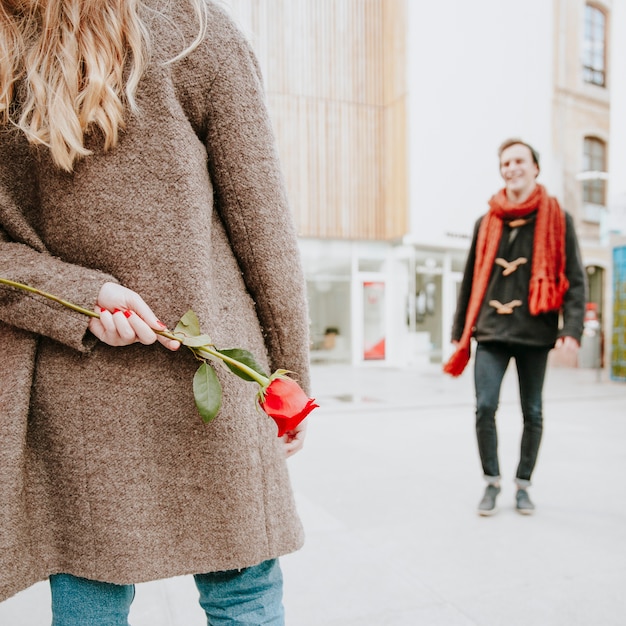 Woman with rose behind back waiting for man