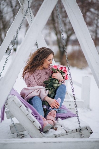 Free photo woman with roses outside in winter sitting on swings