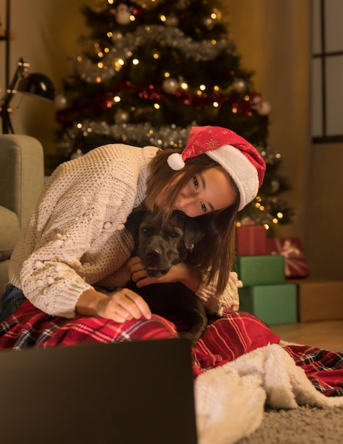 Woman with santa hat and her dog on christmas looking at laptop