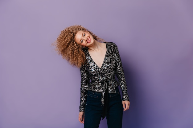 Woman with shiny shadows on her eyelids smiles with her eyes closed. Snapshot of curly girl in sequined blouse.