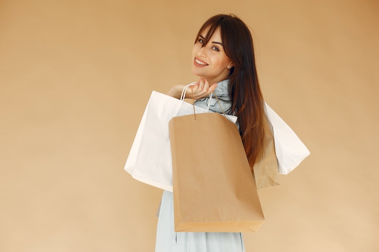 無料Photo 買い物袋を持つ女性。ベージュの壁の女性。青いジャケットの女性。