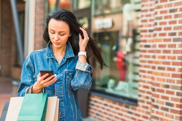 モールでスマートフォンを使用してショッピングバッグを持つ女性