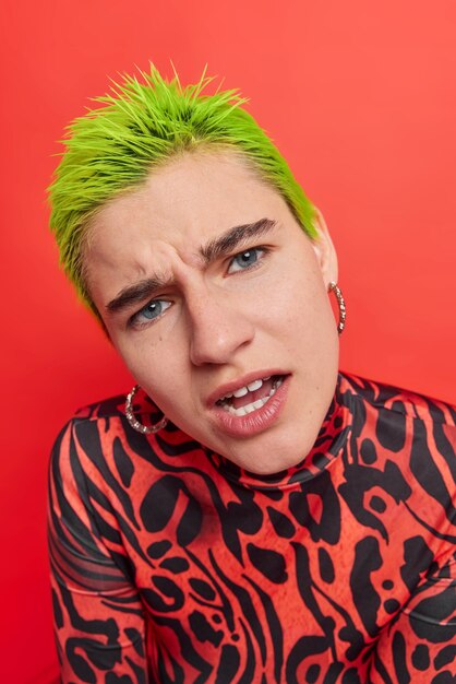 woman with short green hair reacts on something unpleasant hears offensive words wears casual jumper on red