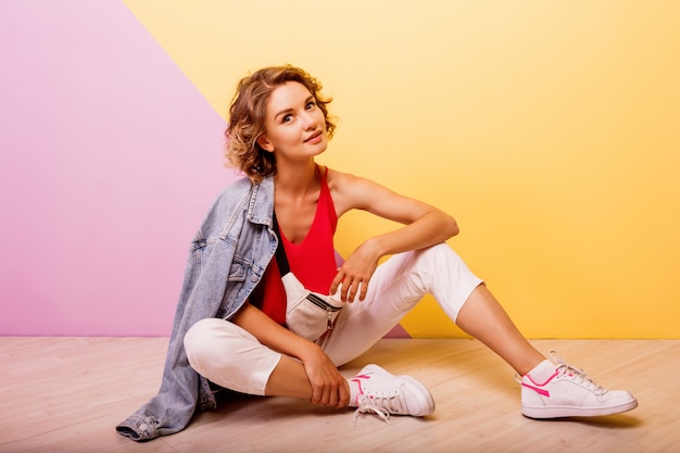 Woman with short wavy hairs  sitting on the floor over pink