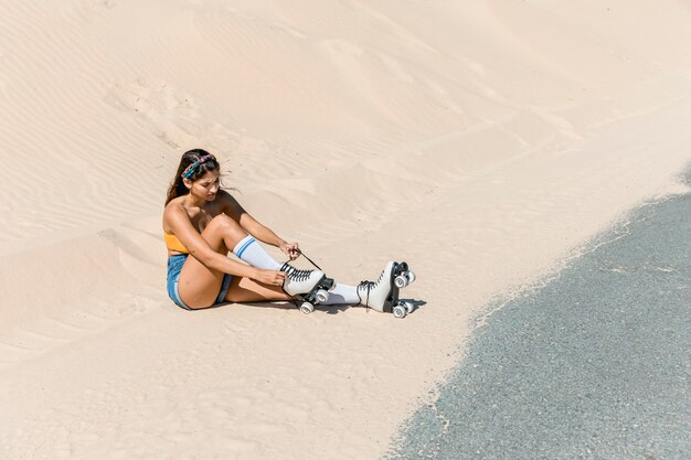 砂の上に座ってスケートを持つ女性