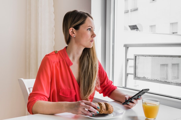 Foto gratuita donna con smarthone che osserva fuori finestra nella caffetteria