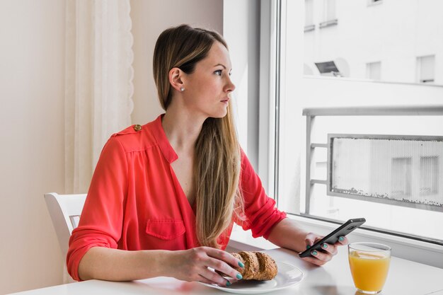 Женщина с smarthone глядя в окно в кафе