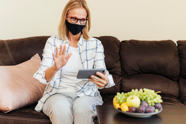 Foto gratuita donna con smartphone e maschera di cotone a casa durante la quarantena